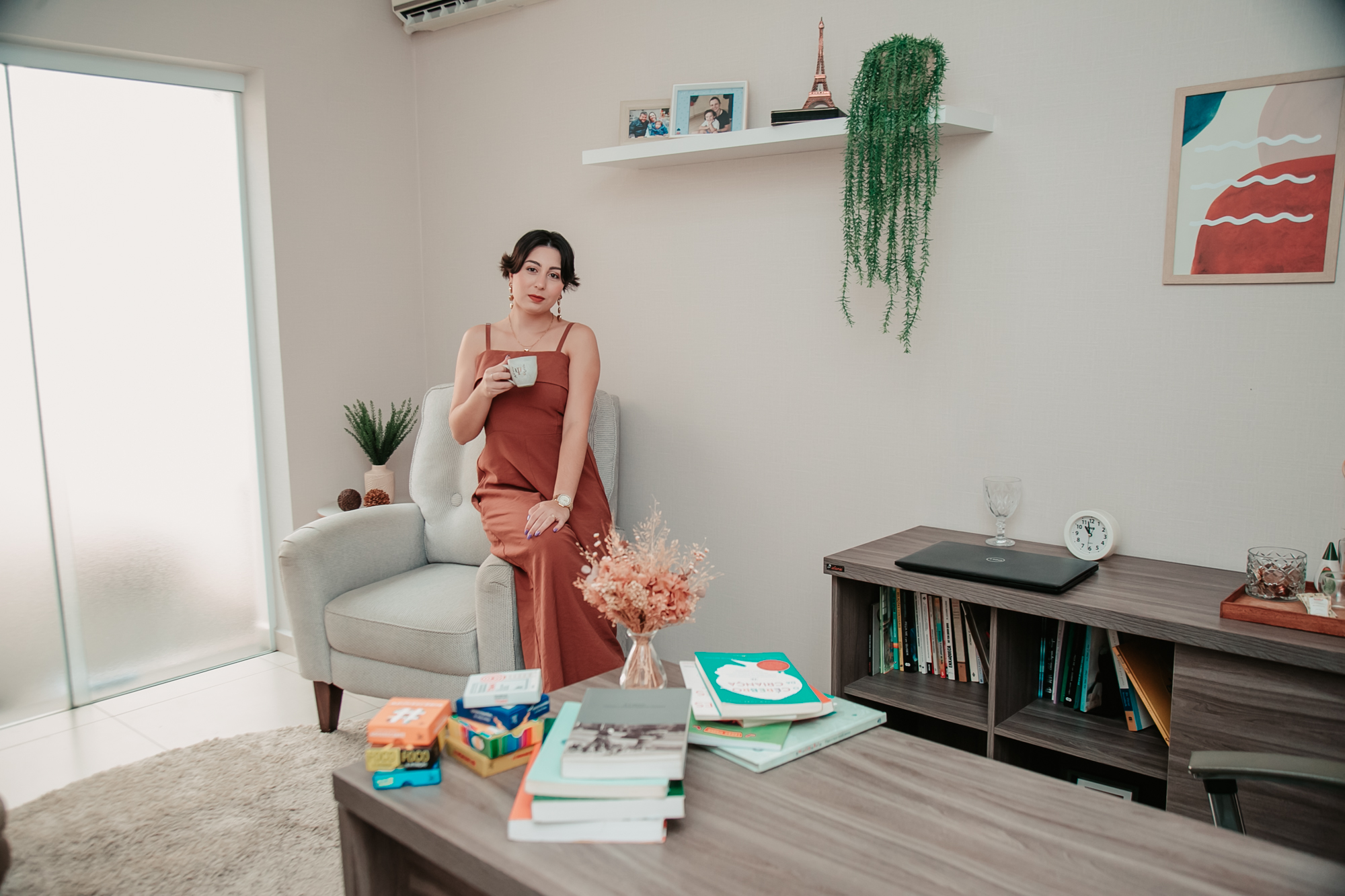Gabriela Barbi no ambiente do consultório, com estante de livros e decoração acolhedora